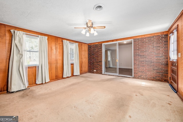 carpeted spare room with a ceiling fan, visible vents, brick wall, and a textured ceiling