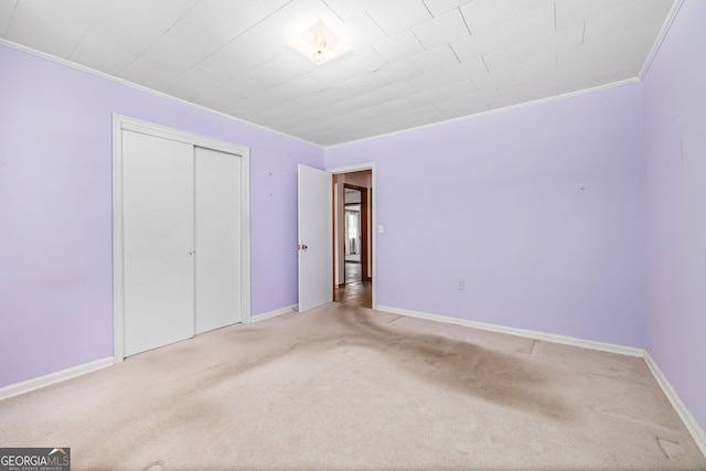 unfurnished bedroom with crown molding, a closet, baseboards, and carpet floors