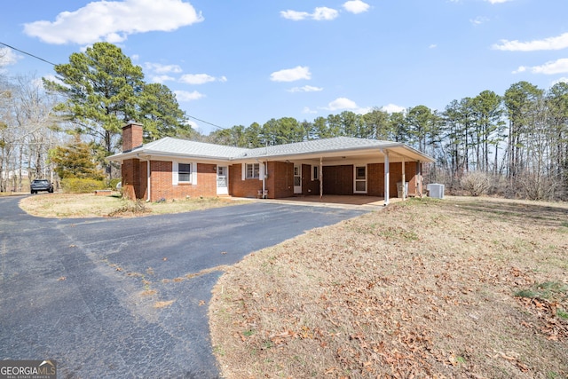 ranch-style home with aphalt driveway, a carport, brick siding, and a chimney