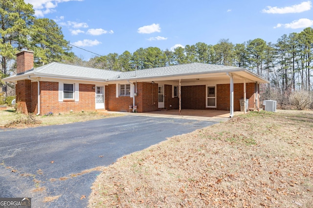 ranch-style home with brick siding, aphalt driveway, central air condition unit, a chimney, and a carport