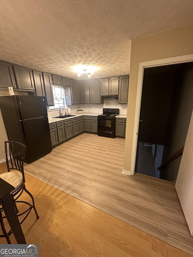 kitchen featuring light wood-type flooring, light countertops, gray cabinets, black appliances, and a sink