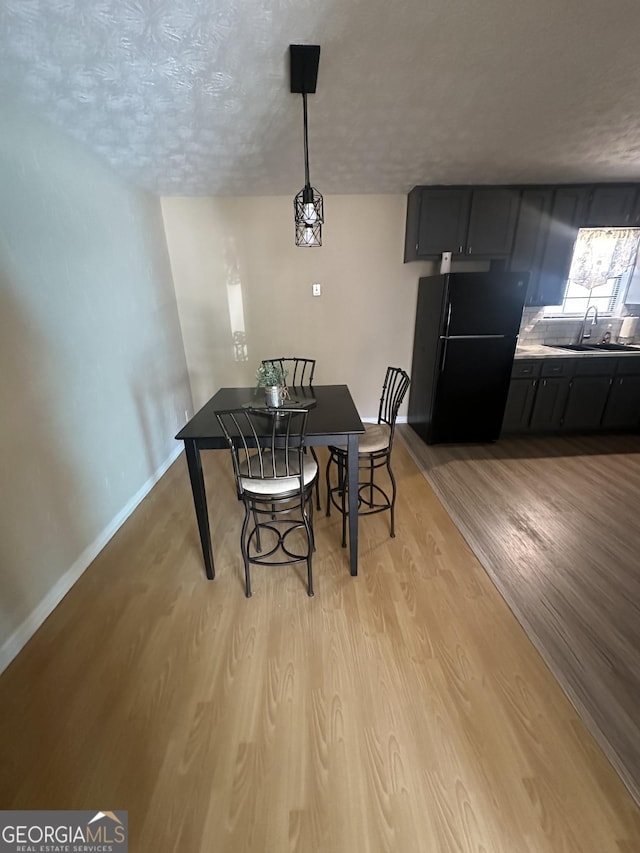 dining room with light wood finished floors, a textured ceiling, and baseboards