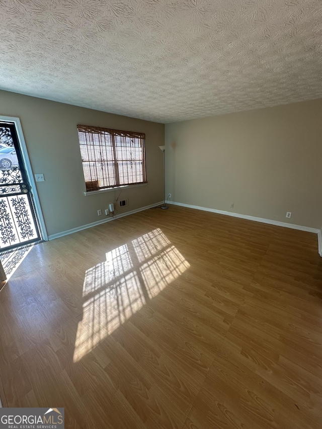 unfurnished living room with visible vents, baseboards, a textured ceiling, and wood finished floors