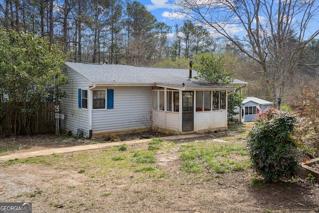 view of front of home with a sunroom, fence, and a shingled roof