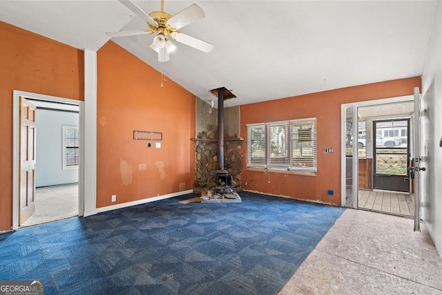 unfurnished living room featuring a wood stove, a ceiling fan, carpet floors, and high vaulted ceiling