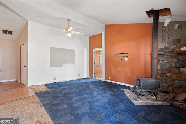 living room featuring visible vents, a wood stove, a ceiling fan, and vaulted ceiling