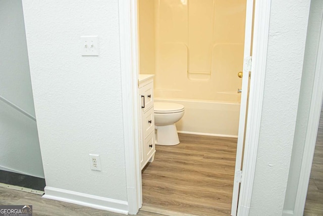 bathroom featuring toilet, wood finished floors, baseboards, vanity, and a textured wall