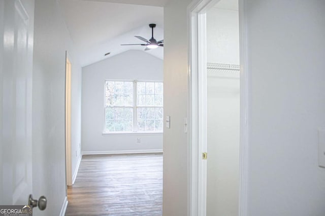 hall with wood finished floors, baseboards, and vaulted ceiling