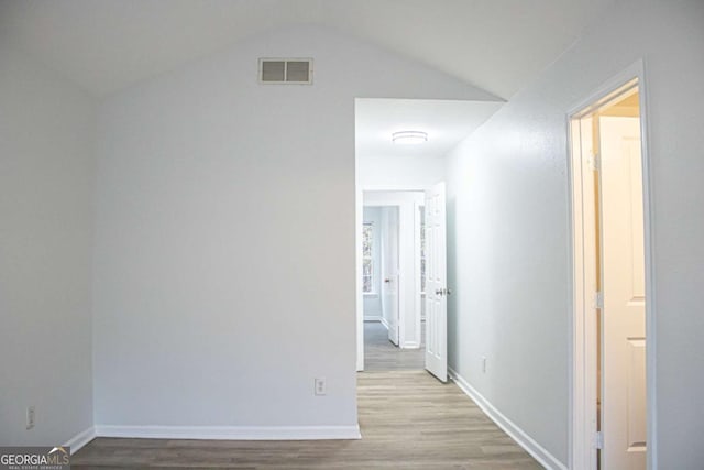 hallway with visible vents, lofted ceiling, baseboards, and wood finished floors