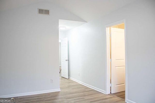 empty room with vaulted ceiling, wood finished floors, visible vents, and baseboards