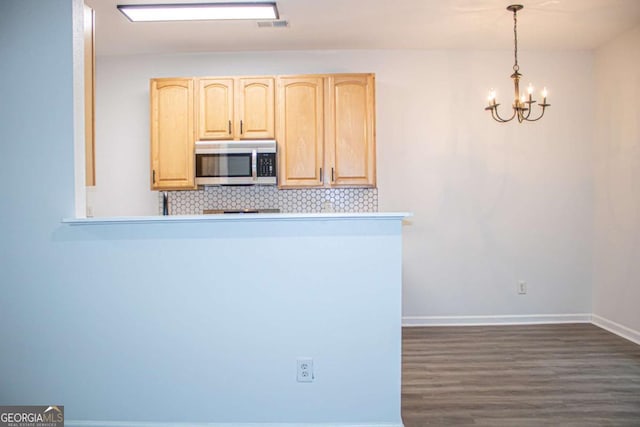 kitchen with dark wood-style floors, light brown cabinets, decorative backsplash, stainless steel microwave, and a chandelier