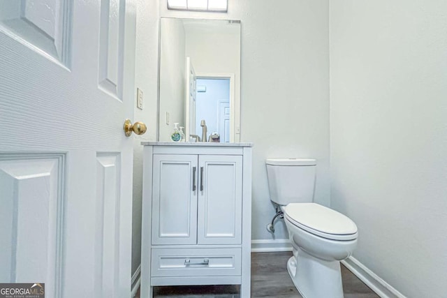 bathroom with baseboards, toilet, wood finished floors, and vanity