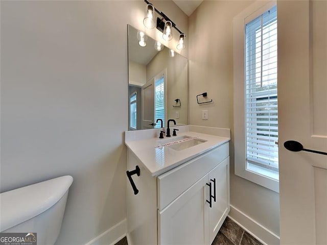 half bathroom with baseboards, plenty of natural light, toilet, and vanity