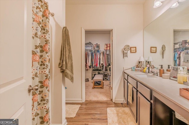 bathroom featuring baseboards, a spacious closet, wood finished floors, and vanity