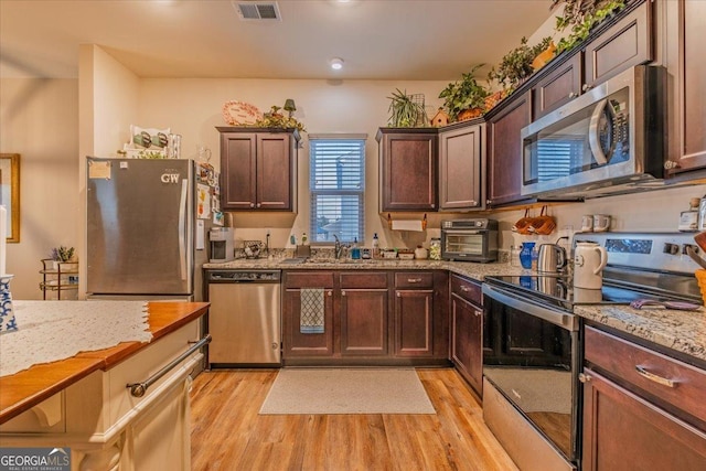 kitchen with visible vents, light stone countertops, appliances with stainless steel finishes, and light wood finished floors