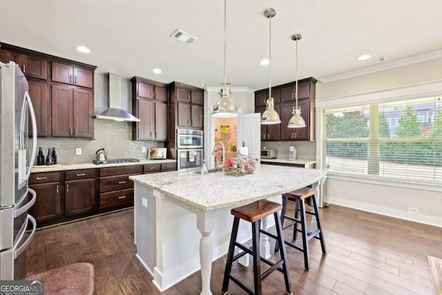 kitchen featuring visible vents, appliances with stainless steel finishes, dark wood-style floors, wall chimney exhaust hood, and a kitchen island with sink