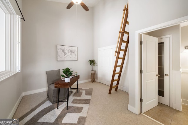 home office featuring light colored carpet, baseboards, a towering ceiling, and ceiling fan