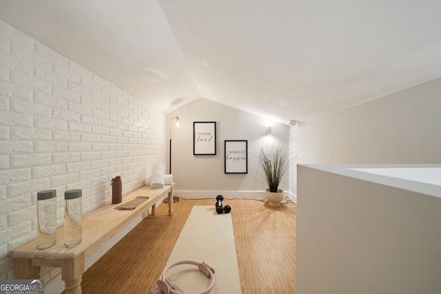 home theater room featuring vaulted ceiling, wood finished floors, baseboards, and brick wall