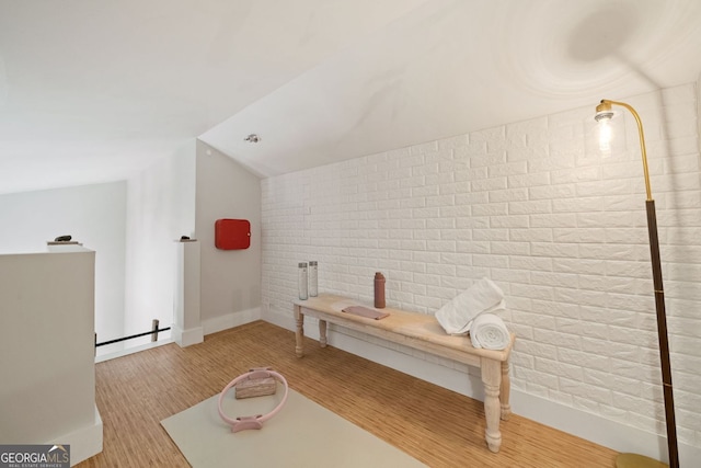 interior space with wood finished floors, a baseboard radiator, lofted ceiling, and brick wall