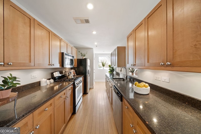 kitchen with light wood finished floors, visible vents, dark stone countertops, stainless steel appliances, and a sink