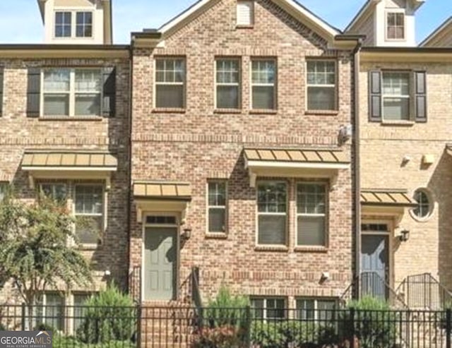 view of property featuring a standing seam roof, brick siding, and a fenced front yard