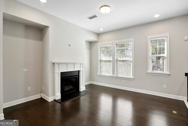 unfurnished living room with a glass covered fireplace, visible vents, baseboards, and dark wood finished floors