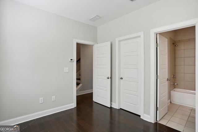 unfurnished bedroom with visible vents, ensuite bathroom, baseboards, and wood finished floors