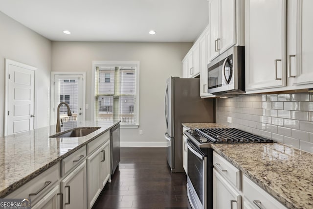 kitchen featuring light stone countertops, dark wood-style flooring, a sink, stainless steel appliances, and tasteful backsplash