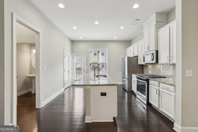 kitchen featuring a center island with sink, a sink, stainless steel appliances, white cabinetry, and backsplash