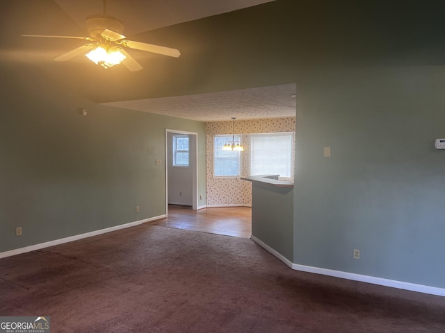 empty room with baseboards, carpet floors, ceiling fan with notable chandelier, and wallpapered walls