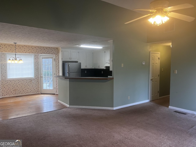 kitchen featuring dark countertops, baseboards, ceiling fan with notable chandelier, freestanding refrigerator, and white cabinets