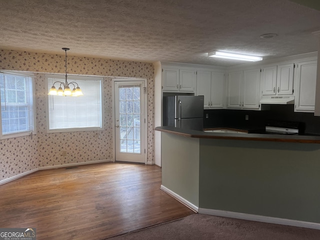 kitchen with under cabinet range hood, dark countertops, wallpapered walls, and freestanding refrigerator