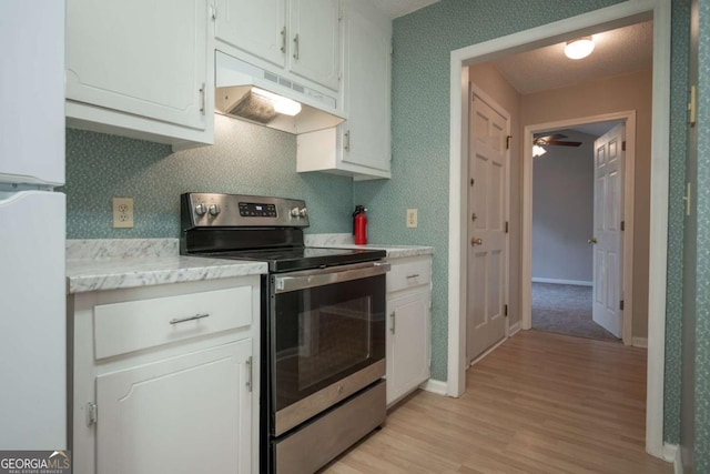 kitchen with under cabinet range hood, light countertops, stainless steel range with electric stovetop, freestanding refrigerator, and white cabinetry