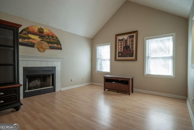 unfurnished living room featuring baseboards, wood finished floors, a tiled fireplace, and vaulted ceiling