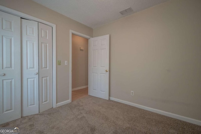 unfurnished bedroom with visible vents, baseboards, a closet, a textured ceiling, and carpet flooring