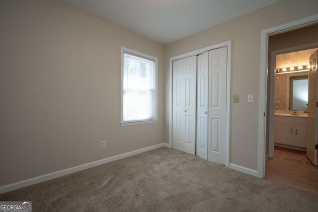 unfurnished bedroom featuring carpet flooring, baseboards, a closet, and a sink