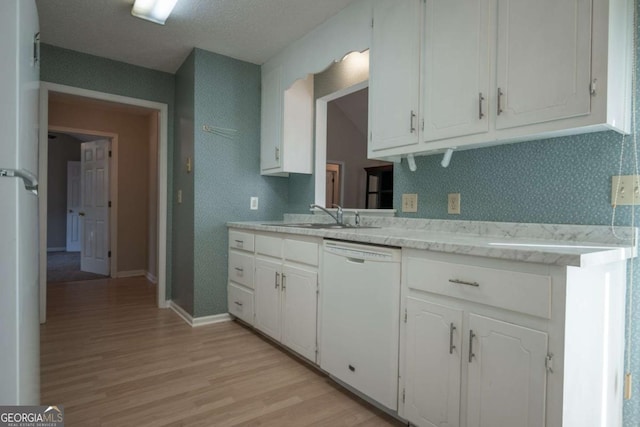 kitchen featuring light wood-type flooring, light countertops, white dishwasher, white cabinets, and a sink