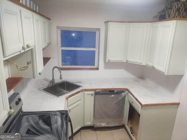 kitchen with stove, light countertops, backsplash, and a sink