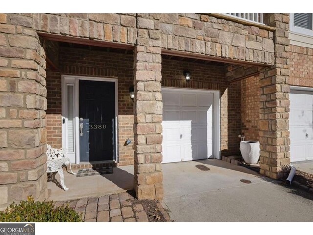doorway to property with concrete driveway, brick siding, and a garage
