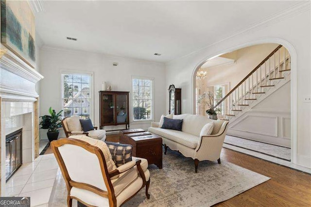 living area featuring ornamental molding, stairway, arched walkways, a decorative wall, and a tile fireplace