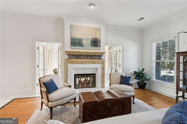 living room with visible vents, ornamental molding, a tiled fireplace, wood finished floors, and baseboards