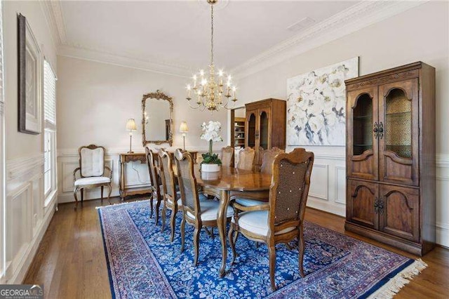 dining room with a wainscoted wall, dark wood-style flooring, a chandelier, and crown molding