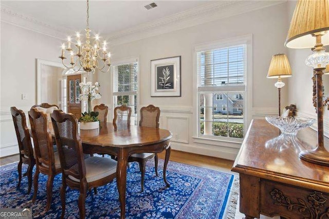 dining space with wood finished floors, visible vents, ornamental molding, wainscoting, and a notable chandelier