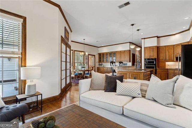 living room featuring visible vents, wood finished floors, crown molding, baseboards, and a chandelier