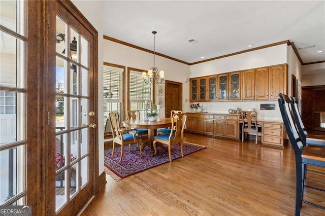 dining space with visible vents, light wood-style flooring, an inviting chandelier, and ornamental molding