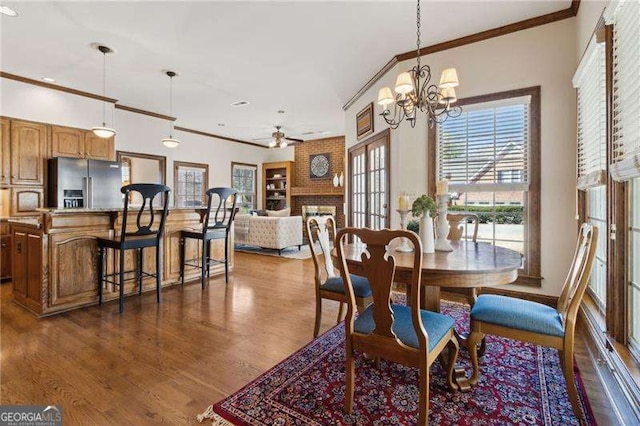 dining space featuring ceiling fan with notable chandelier, dark wood-style floors, a fireplace, crown molding, and baseboards