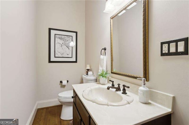 bathroom featuring baseboards, toilet, wood finished floors, and vanity