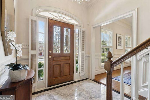 foyer entrance with a wainscoted wall, marble finish floor, crown molding, and a decorative wall