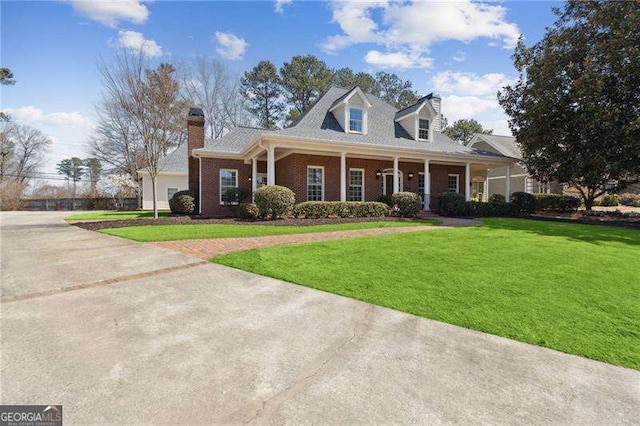 cape cod home with a front yard, driveway, a porch, a chimney, and brick siding