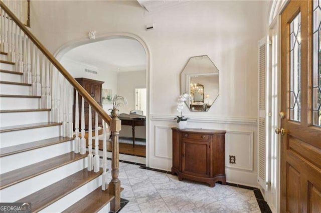 foyer entrance with visible vents, arched walkways, stairs, wainscoting, and a decorative wall